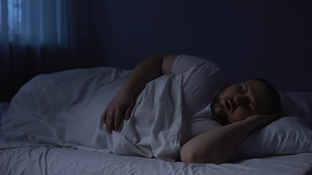 Male snoring at night in bed, sleeping apnea disease, breath shortness, asthma