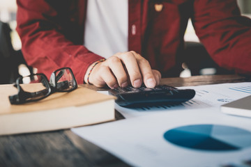 Close up of businessman or accountant hand holding pencil working on calculator to calculate financial data report, accountancy document and laptop computer at office, business concept