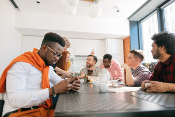 young african guy with mobile phone ignoring his co-workers birthday. introvert in the collective