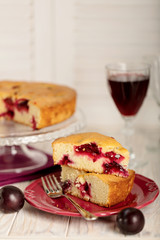 Homemade plum cake on a glass stand and red wine.
