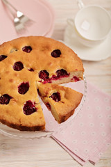 Homemade plum cake on a glass stand and pink plates.