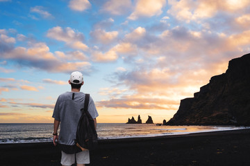 a man with backpack standing on black sand beach in sunset, Iceland. Vacation travelling in summer and summer recreation pursuit concept