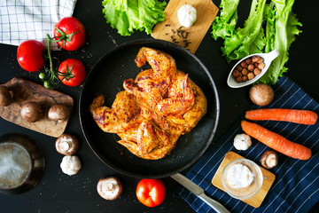 Chicken of tobacco in a frying pan on a black background. The process of preparing a dinner with ingredients