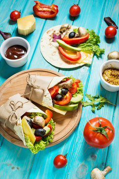Healthy vegan lunch snack. Tortilla wraps with mushrooms, fresh vegetables and Ingredients on blue wooden background