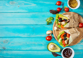 Healthy vegan lunch snack. Tortilla wraps with mushrooms, fresh vegetables and Ingredients on blue wooden background.