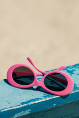 Sunglasses of pink color on the beach.