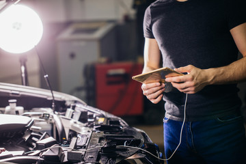 male mechanic using digital tablet next to an open hood in garage