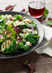 Grilled Zucchini salad with feta cheese, walnut nuts and glass of red wine in a black plate on wooden table