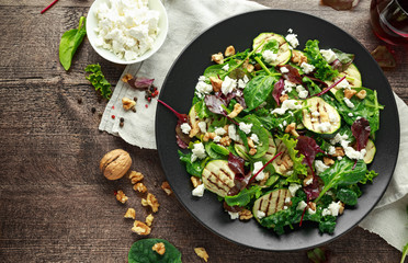 Grilled Zucchini salad with feta cheese, walnut nuts and glass of red wine in a black plate on wooden table © grinchh
