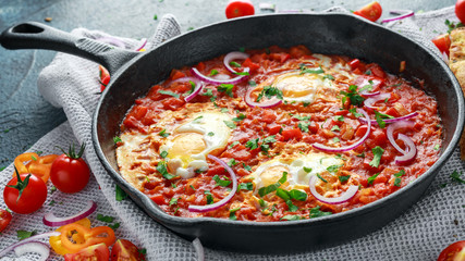 Tasty Breakfast Shakshuka in a Iron Pan. Fried eggs with tomatoes, red, yellow peppers, onion, parsley, Pita bread and herbs. Healthy Food