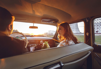 Young wedding couple sitting smiling inside retro car and looking at each other. just married embrace is hugging inside car. bride hugging groom who is driving the car. Wedding with retro car.