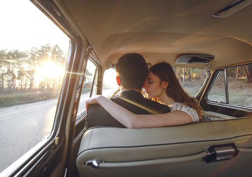 Young wedding couple sitting smiling inside retro car. just married embrace is hugging inside car. bride hugging groom who is driving the car. Wedding with retro old car