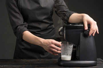 A professional barista with a coffee machine, makes foam from milk for latte. Against a dark background