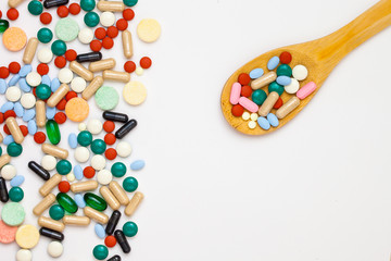 Assorted pharmaceutical medicine pills, tablets and capsules over white background with a few on a wooden spoon