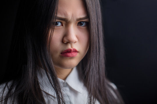 Close up of displeased asian woman with frowny face and resentful look against black background
