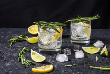 Alcoholic drink gin tonic cocktail with lemon, rosemary and ice on stone table