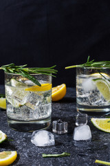 Alcoholic drink gin tonic cocktail with lemon, rosemary and ice on stone table