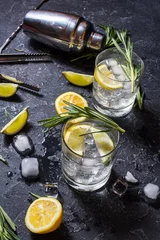 Tuinposter Alcoholische drank gin tonic cocktail met citroen, rozemarijn en ijs op stenen tafel © voloshin311