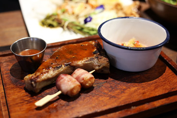 Pork chops steak with side dishes such as sausage wrapped bacon, pineapple salsa and barbecue sauce.