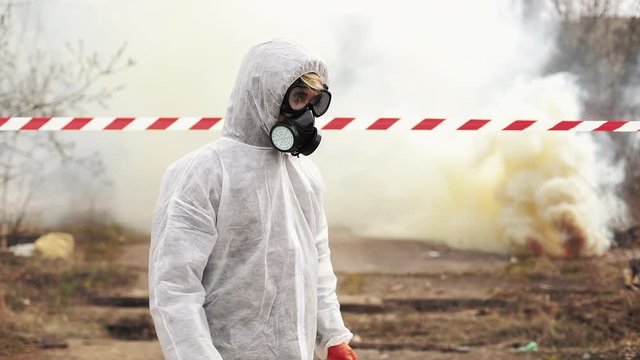 Man in bio-hazard suit and gas walks to the polluted zone covered with smoke