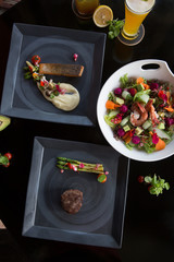 Various different dishes on dark background. Fish, steak, salad