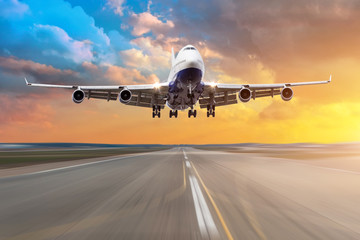Airplane with four engines flying arrival landing on a runway in the evening during a bright red...
