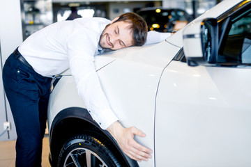Emotional happy man hugging his new car in showroom