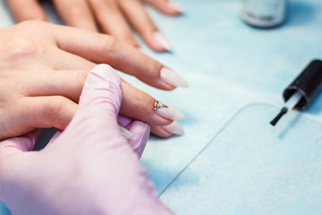 Obraz na płótnie Canvas Close up manicure process. A professional manicurist glues rhinestones on nails