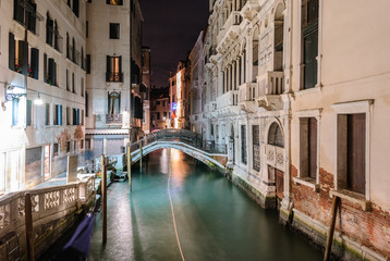 Fototapeta na wymiar Night view of a typical canal in Venice with the light trail of a boat