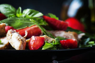 Salad with arugula, strawberries and chicken, dark background, selective focus