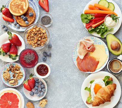 Breakfast food table. Festive brunch set, meal variety with granola, fried egg, pancakes, croissants, smoothie ,fresh vegetables, berries and fruits. Overhead view, copy space