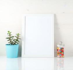 White frame, succulent, candy on white table against the white wall. Mockup with copy space in Scandinavian style