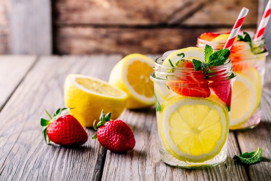 Lemon and strawberry lemonade in glass mason jars on a wooden background.