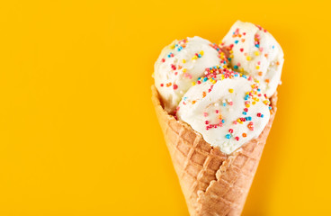 ice cream balls with colored sugar sprinkles in a Waffle Cone on a yellow Background. Vanilla ice cream in a waffle cone.