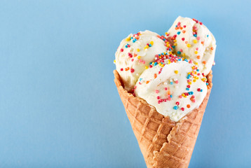 ice cream balls with colored sugar sprinkles in a Waffle Cone on a Blue Background. Vanilla ice...
