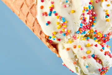Obraz na płótnie Canvas ice cream balls with colored sugar sprinkles in a Waffle Cone on a Blue Background. Vanilla ice cream in a waffle cone.
