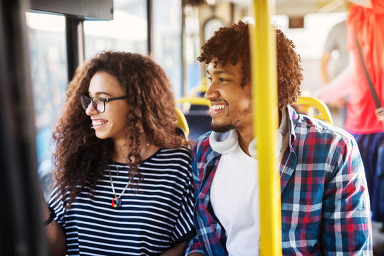 Young cheerful happy couple is sitting in a bus and smiling while looking trough the window. - Powered by Adobe