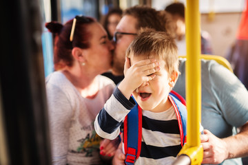 Young happy couple is showing affection through a kiss in a bus while their young adorable little toddler is facepalming because of second hand shame. © Dusan Petkovic