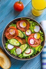 Vegan healthy breakfast on a blue blue table - salad with tomatoes, cucumber and radish and olive oil, orange juice and toasted bread