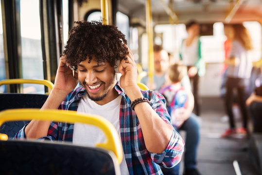 Young cheerful handsome man is adjusting his headset and enjoying the bus ride.