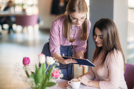 Attractive young waitress using a tablet computer to take an order from a customer in a coffee shop