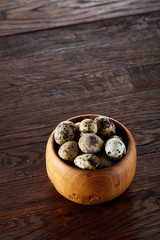 Fresh quail eggs in a wooden bowl on a dark wooden background, top view, close-up
