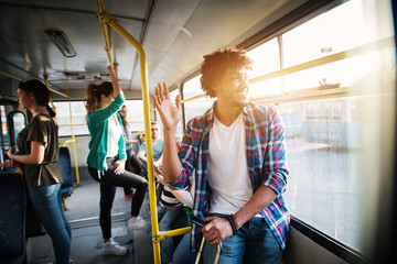 Young joyful handsome man is standing in the bus leaning against the bar and waving to someone...
