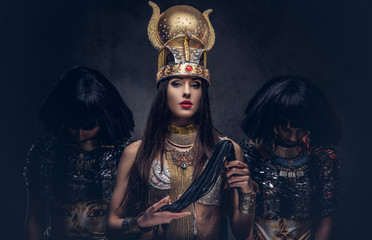 Portrait of haughty Egyptian queen in an ancient pharaoh costume with two concubines.