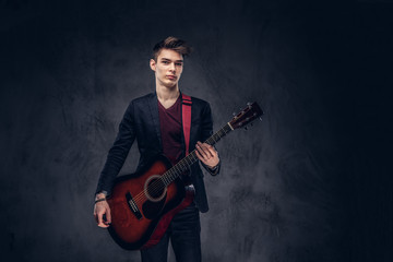 Stylish young musician with stylish hair in elegant clothes posing with a guitar in his hands. Isolated on a dark background.