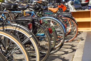 Row of city bicycles parked in a paved street.Selective focus on the first wheel