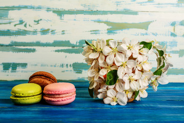 Multicolored macaroons and cup decorated with white flowers of apple trees on a blue wooden background.