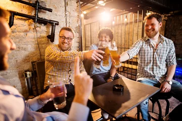 Printed kitchen splashbacks Bar Cheerful male friends clinking with draft beer in front of their friend with a glass of water in hand and rejecting alcohol.