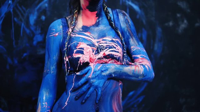The sexy girl blurs the blue and pink paint erotically on her body, touches herself. Pink paint splash from the side. Slow motion