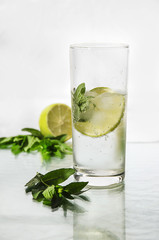 Cold fresh water with bubbles, lime, ice and mint in glass on white background